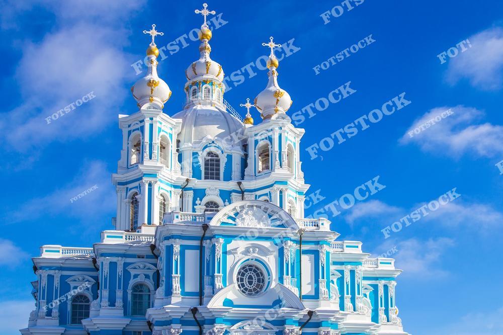 На снимке изображён Смольный собор — один из шедевров барокко в Санкт-Петербурге, построенный по проекту архитектора Растрелли. Золотые купола собора блестят на фоне яркого голубого неба, подчёркивая красоту и изящество архитектурных линий. Светлый день создаёт ощущение лёгкости и торжественности, делая Смольный собор настоящей жемчужиной петербургского пейзажа.
